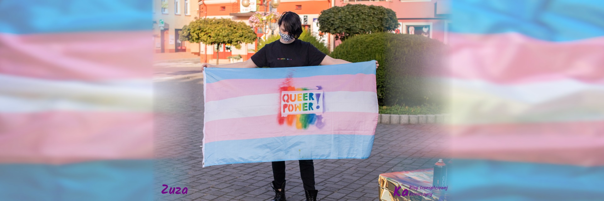 Zuza, ubrana na czarno, na koszulce kolorowe gwiazdki 5 i 3 szt., trzyma flagę trans z tęczowym napisem Queer Power!